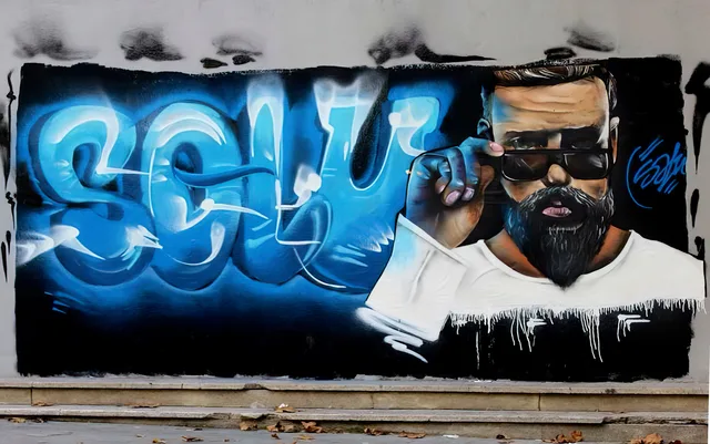 Blauwe SOLU-letters rond een portret van een man met een baard op een buitenmuur.