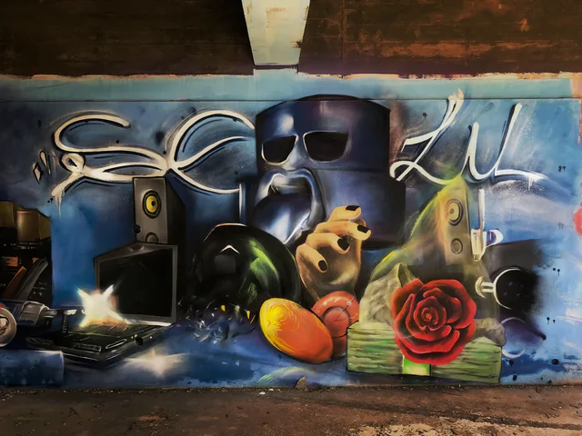 Een surrealistisch geschilderd stilleven met een donkere figuur, fruit en een rode roos in een vervallen gebouw.